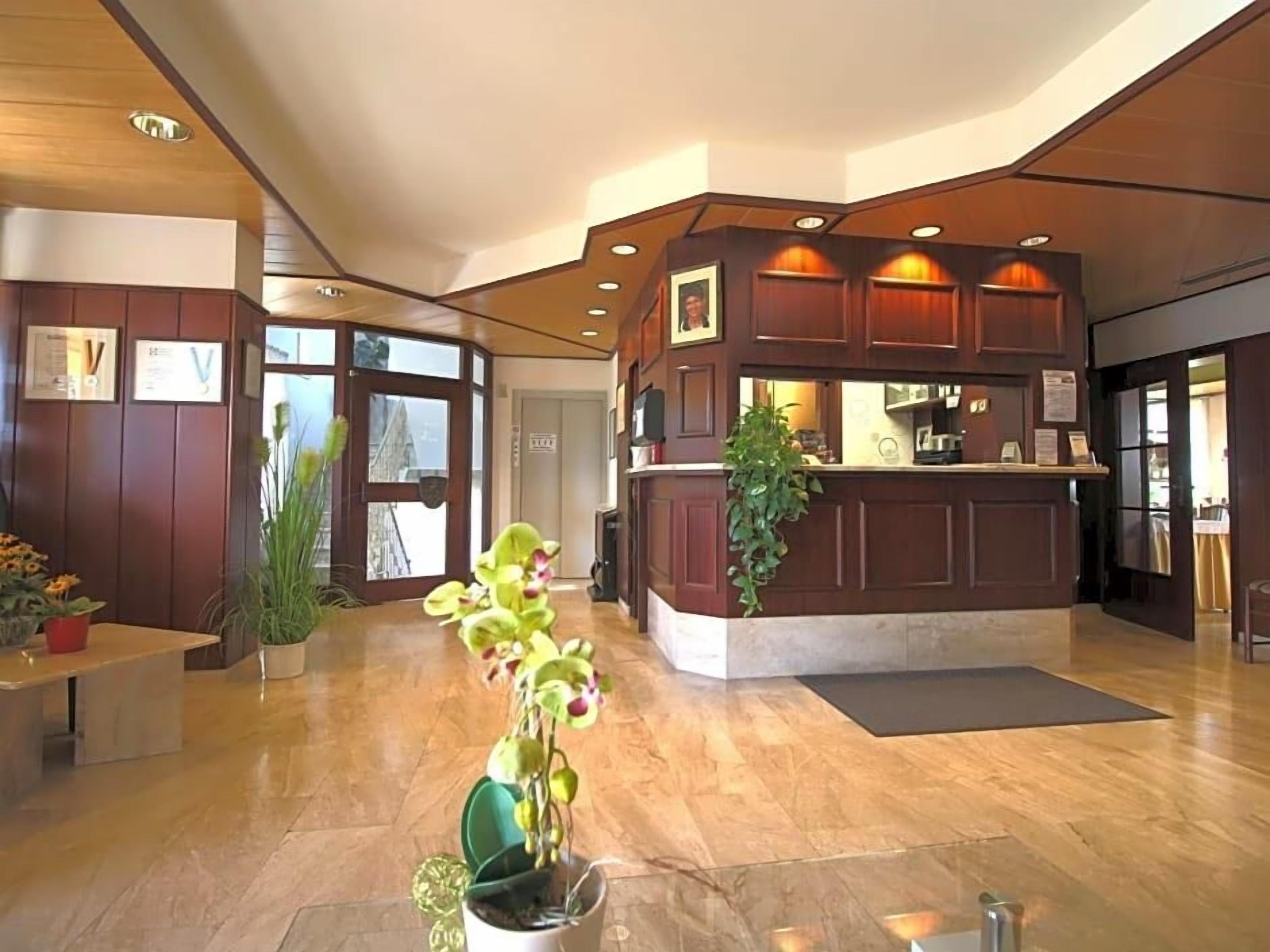 A reception area with a wooden reception desk, potted plants, and a marble floor.