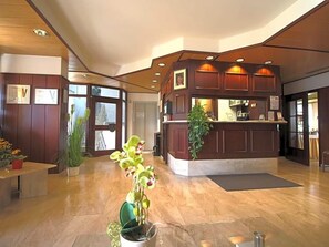 Un espace d’accueil avec un comptoir en bois, des plantes en pot et un sol en marbre.