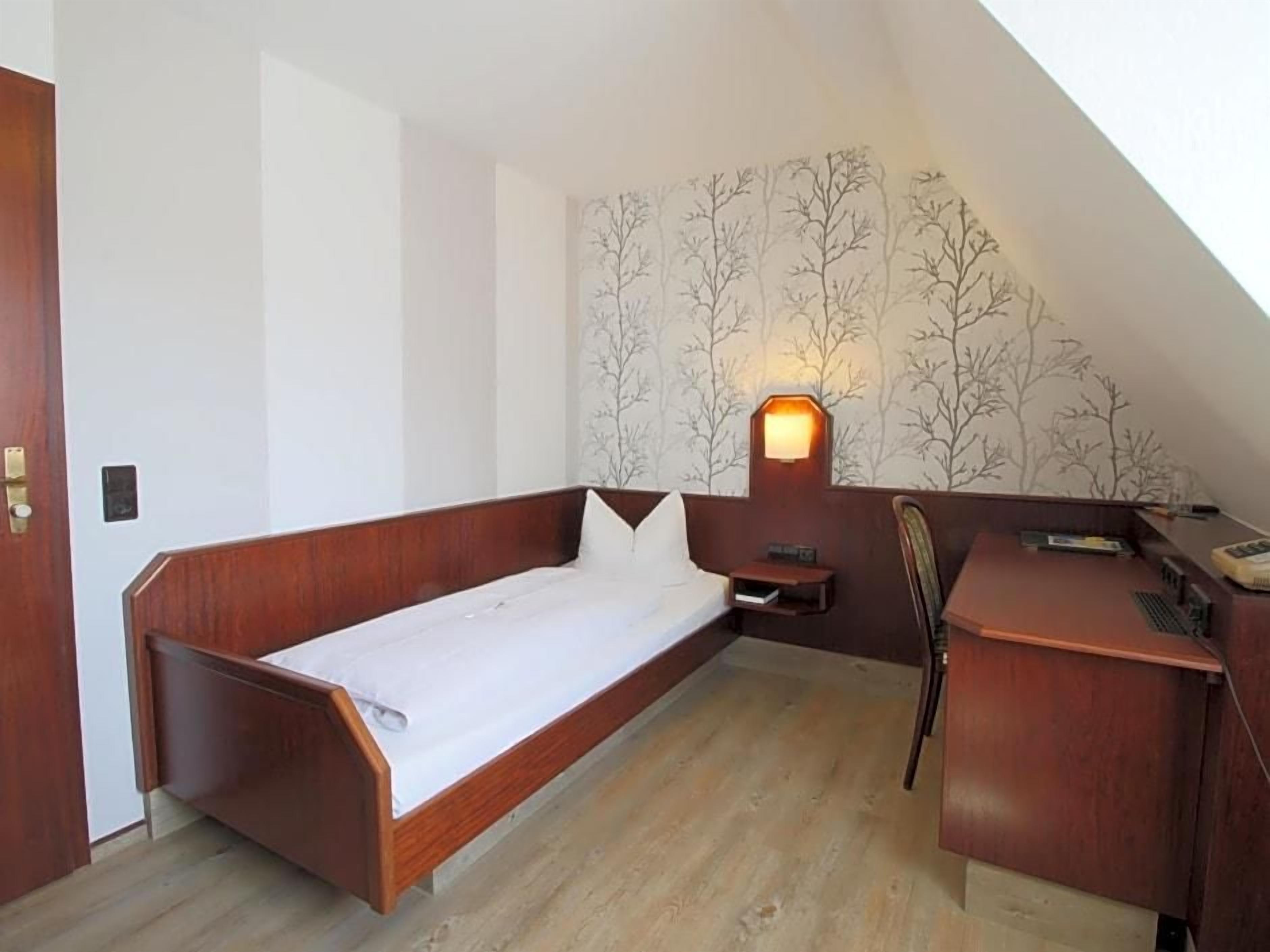 Una habitación con cama, escritorio y lámpara de pared.