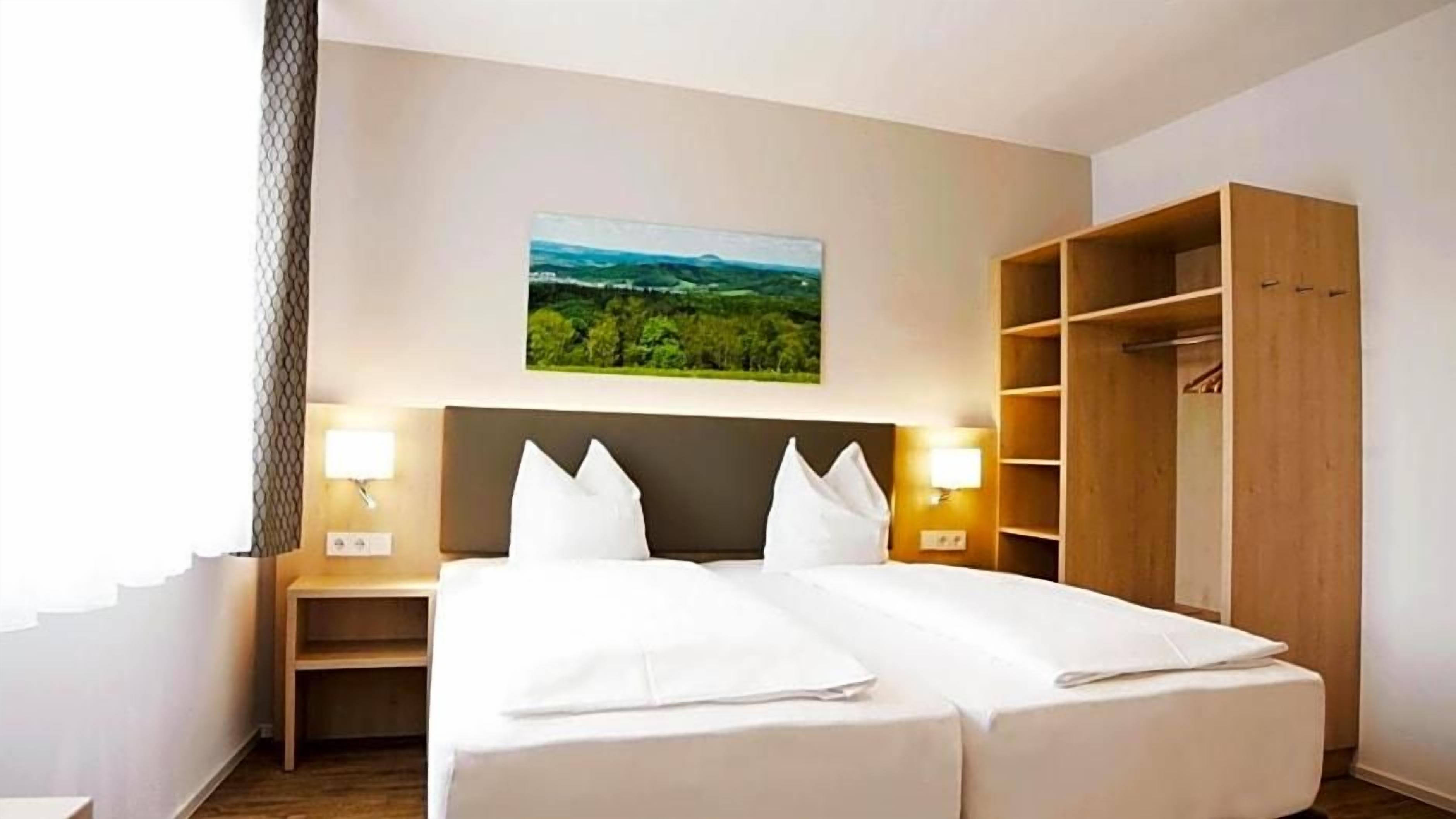 A hotel room with a bed, two bedside tables, a wardrobe, and a landscape painting on the wall.