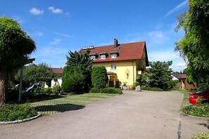 Un hôtel avec un toit rouge, une façade jaune et une allée pavée menant à l’entrée.