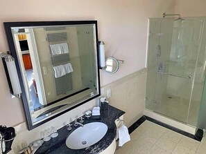 Et badeværelse med et stort spejl, en vask, en glasbrusekabine og en bøjle til håndklæder.