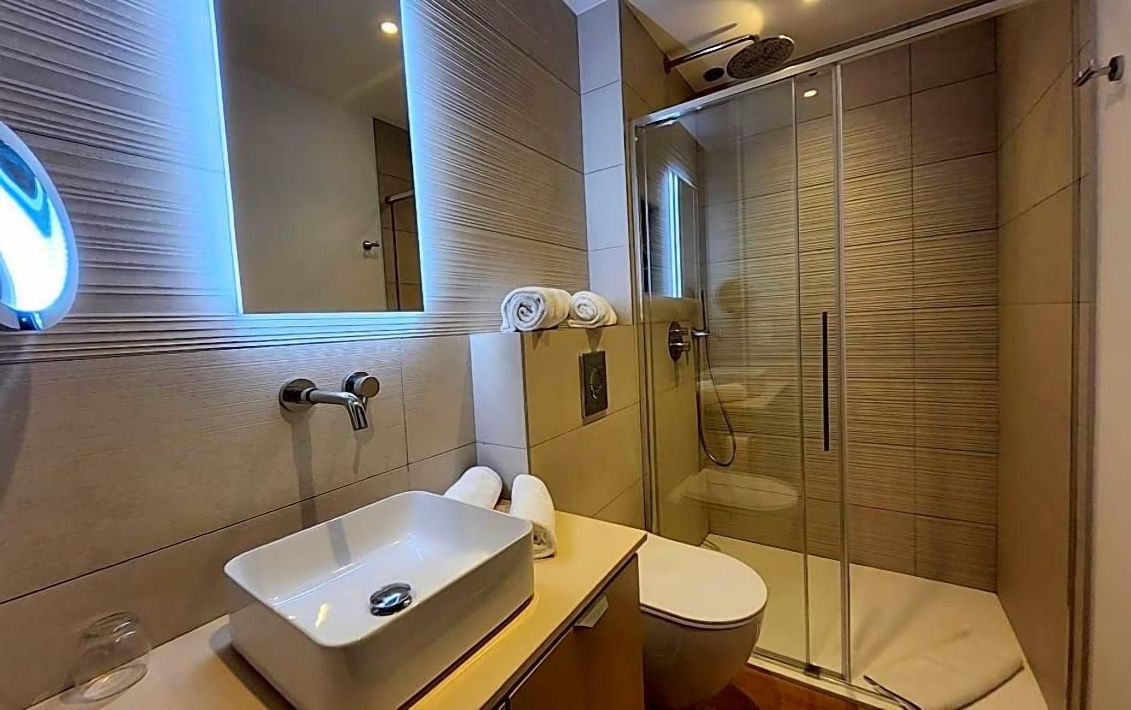 A modern bathroom with a glass-enclosed shower, a white sink, and a toilet.