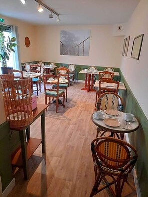 Un restaurante con varias mesas y sillas, suelo de madera y una pared de acento verde.