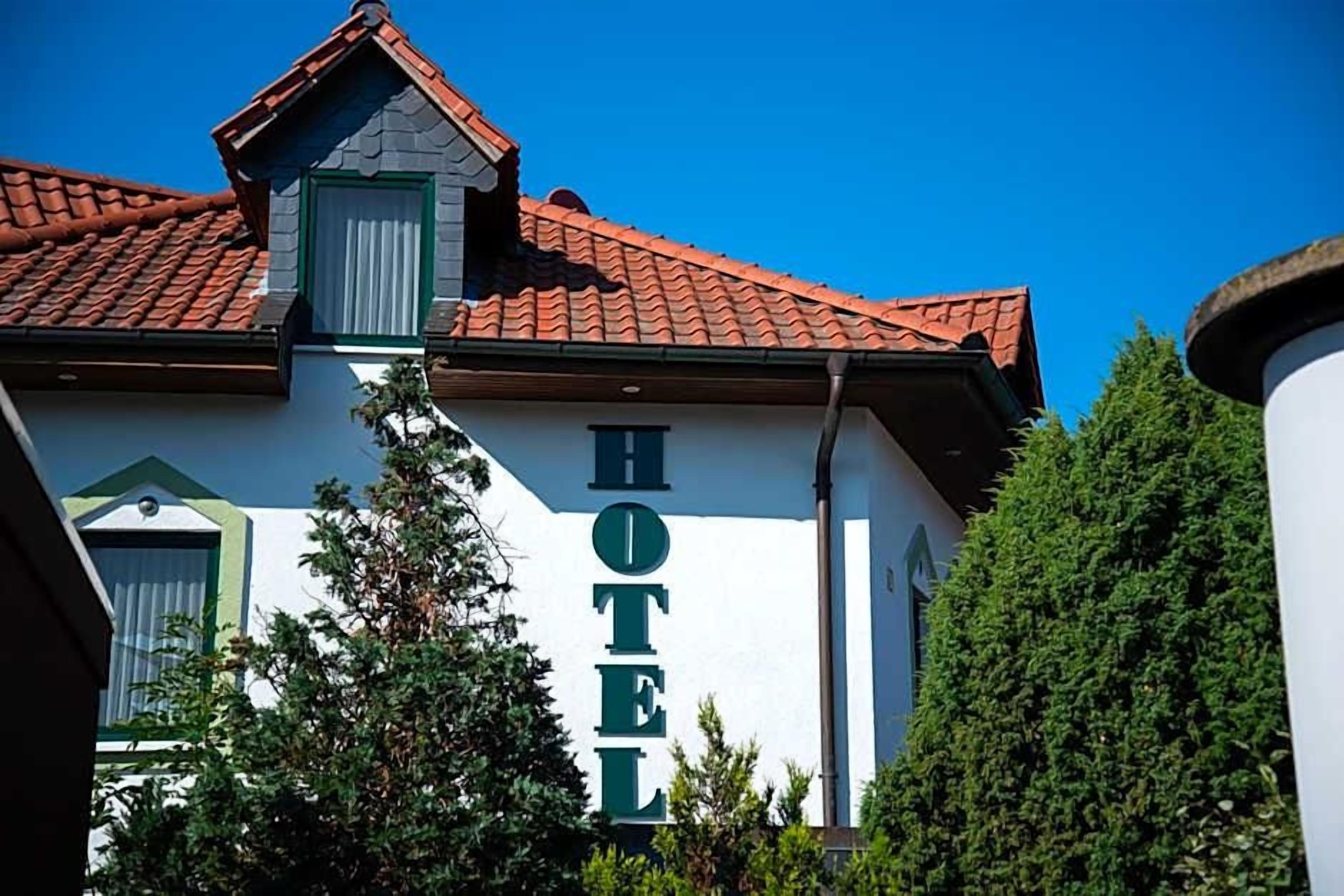 A hotel with a prominent 'HOTEL' sign on the facade, a red-tiled roof, and a green window trim.