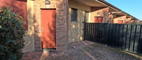 Un edificio residencial con fachada de ladrillo, una puerta roja y un camino de entrada pavimentado.