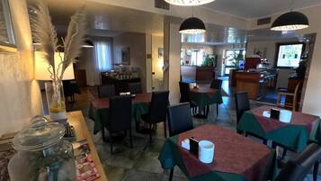 Ein Restaurant mit Tischen, die mit grünen Tischdecken bedeckt sind, schwarzen Stühlen und Pendelleuchten.