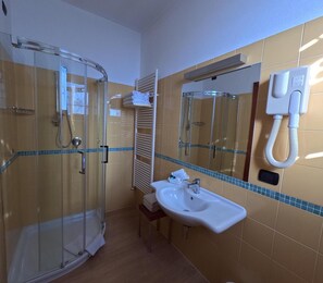 Een badkamer met een glazen douchecabine, een wastafel met spiegel en een handdoekrek.