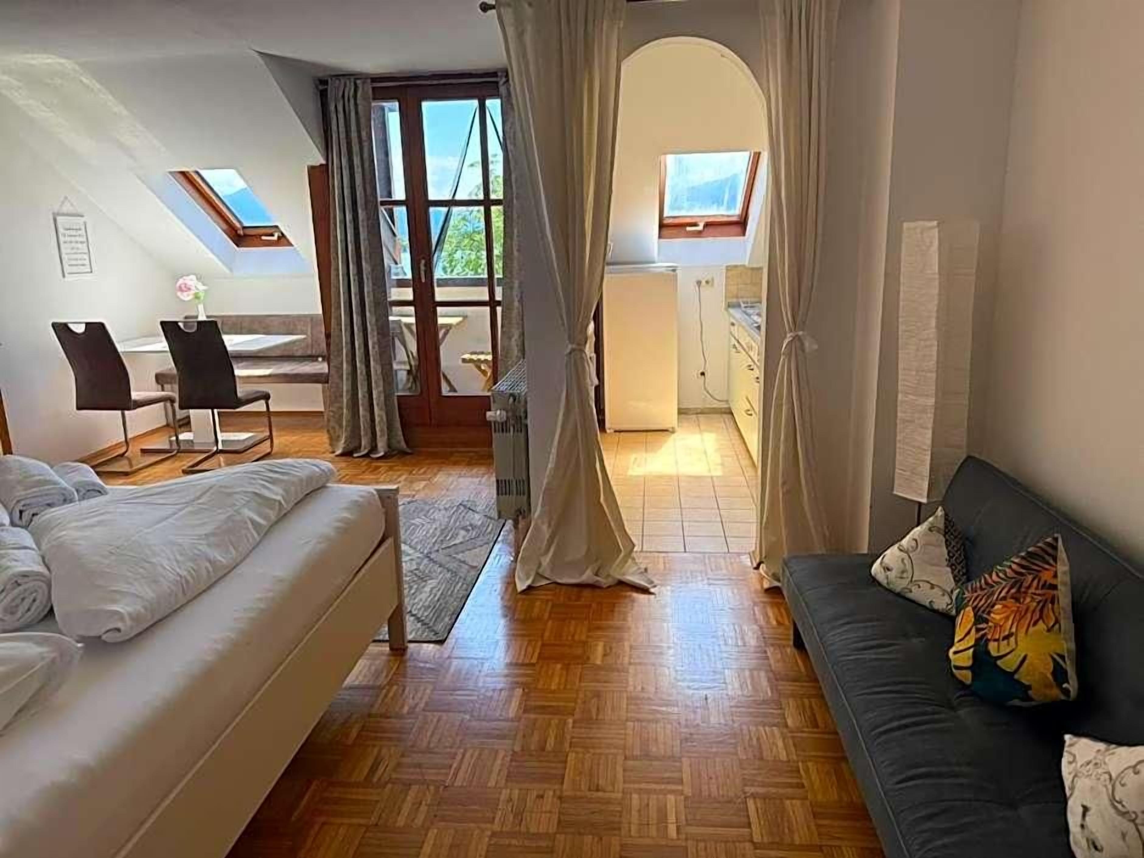 Ett rum med en säng, en soffa, ett matbord med stolar, en köksdel och utsikt genom en dörröppning.