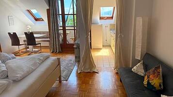 Ein Zimmer mit einem Bett, einem Sofa, einem Esstisch mit Stühlen, einer Küchenzeile und Blick durch eine Tür.