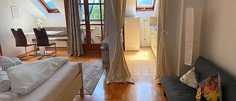 Ett rum med en säng, en soffa, ett matbord med stolar, en köksdel och utsikt genom en dörröppning.