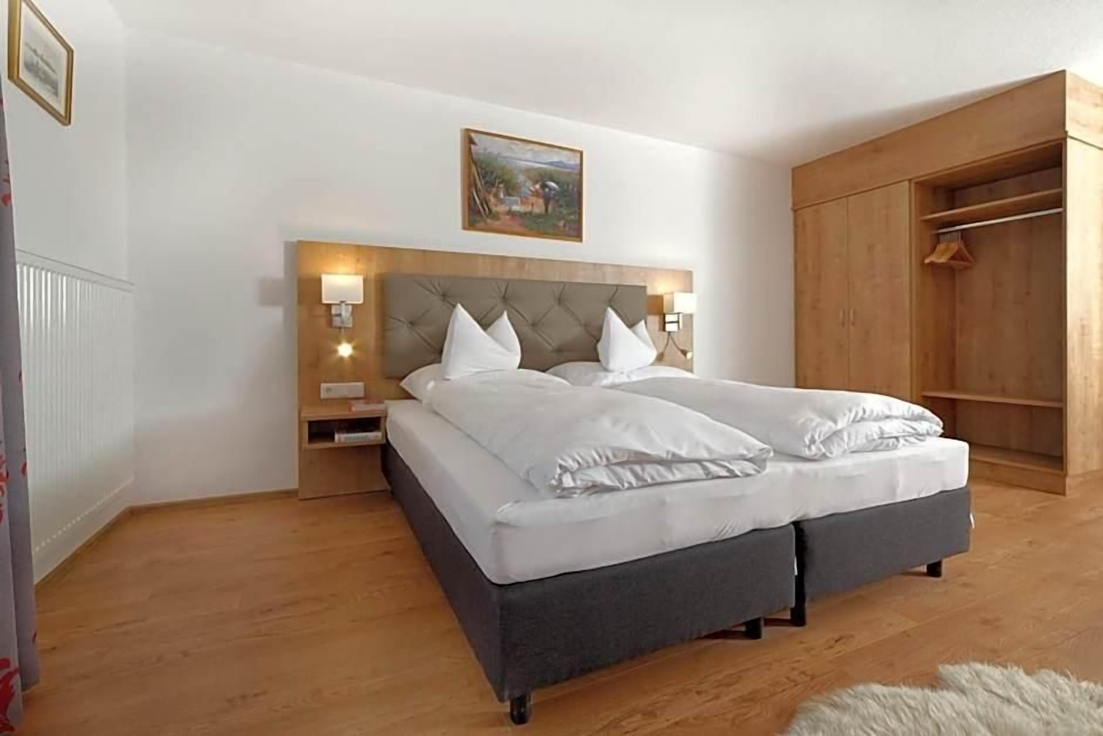 Ein Schlafzimmer mit einem Doppelbett, Nachttischlampen, einem hölzernen Kopfteil, einem Kleiderschrank und einem Gemälde an der Wand.