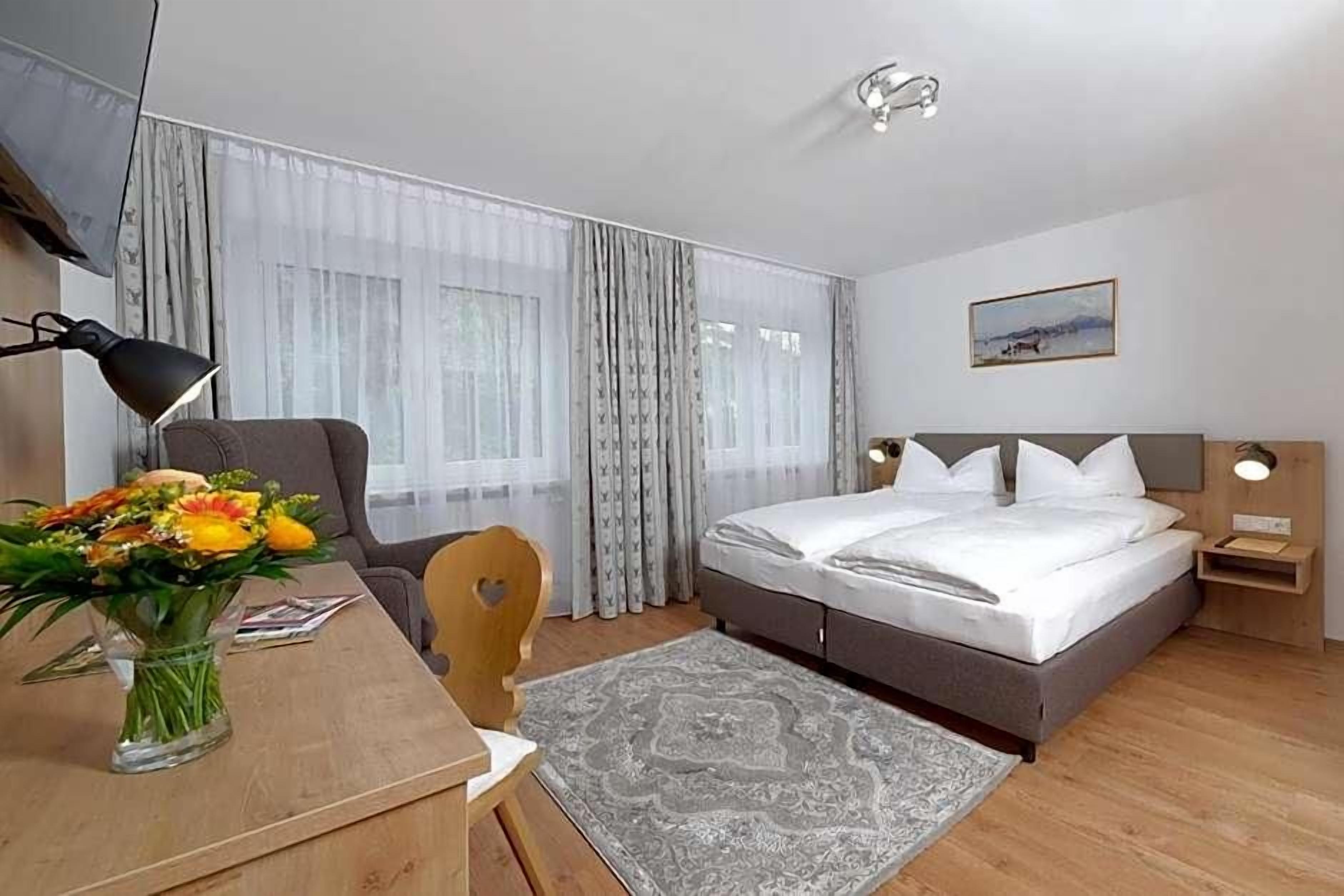 Ein Hotelzimmer mit einem Bett, einem Schreibtisch mit Stuhl, einer Blumenvase, einer Lampe und einem Bild an der Wand.