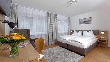 Ein Hotelzimmer mit einem Bett, einem Schreibtisch mit Stuhl, einer Blumenvase, einer Lampe und einem Bild an der Wand.