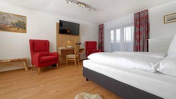 Ein Schlafzimmer mit einem Bett, zwei roten Stühlen, einem Holztisch, einem Fernseher und einem Bild an der Wand.