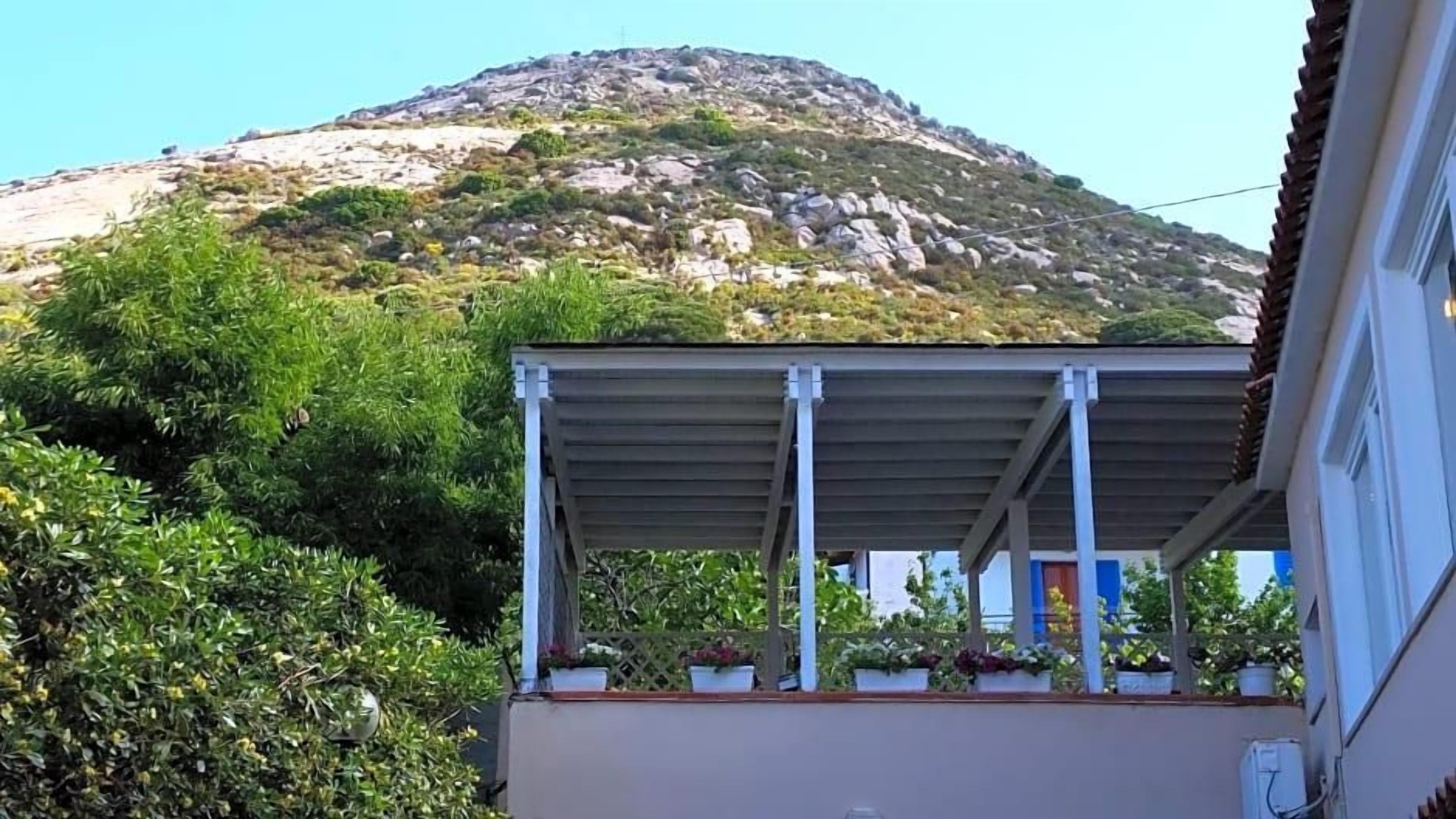 Un edificio con un balcone coperto, piante in vaso e montagne sullo sfondo.