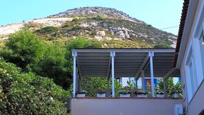 A building with a covered balcony, potted plants, and a mountainous backdrop. - Hotel L'ogliera (Marciana)