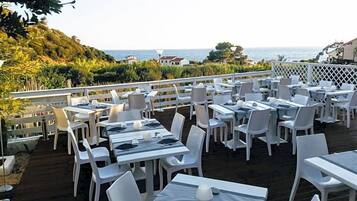 Un'area pranzo all'aperto con tavoli e sedie, con vista sul paesaggio costiero.