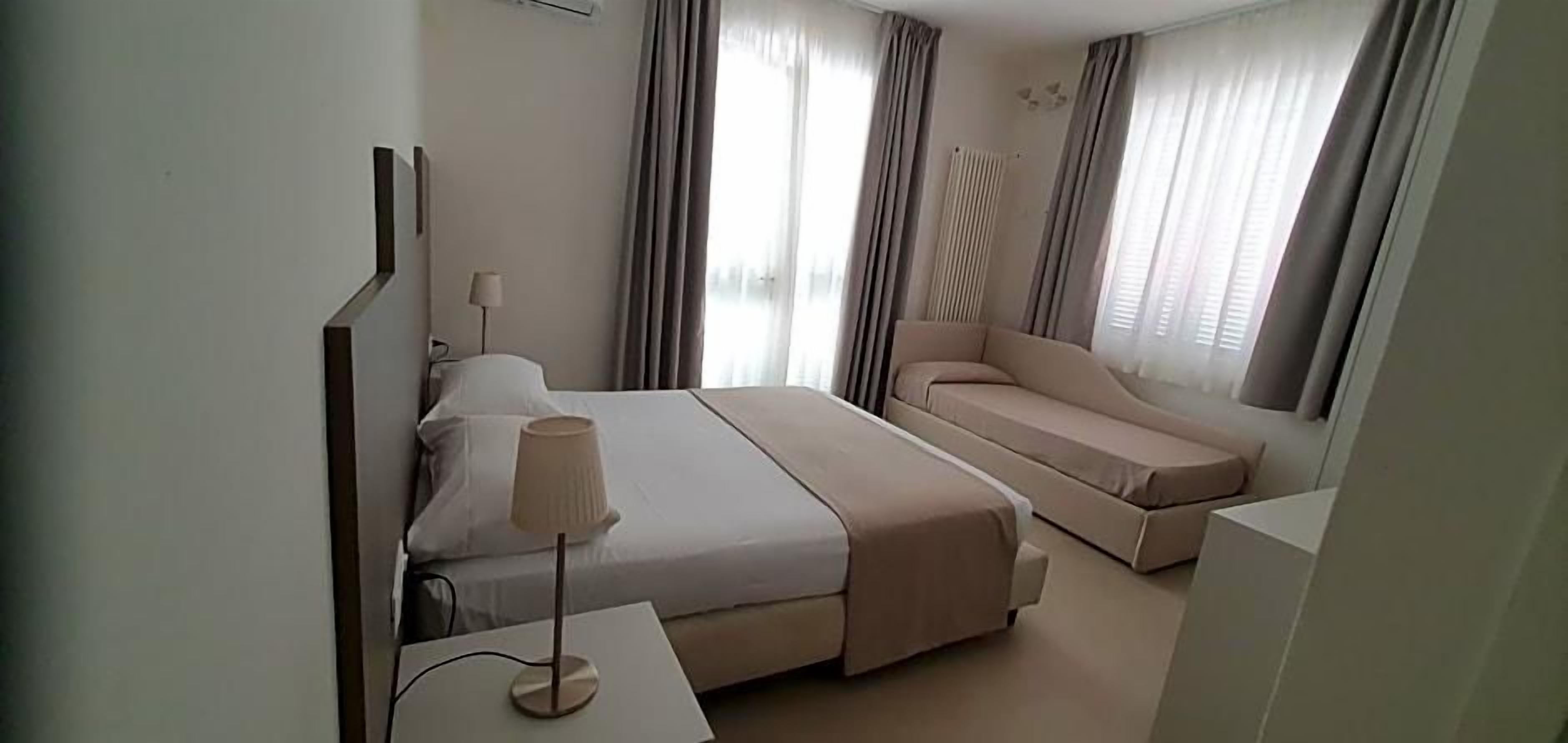 Una camera d'albergo con un letto, un divano, una lampada e una finestra con tende.