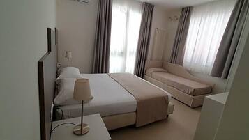 Una camera d'albergo con un letto, un divano, una lampada e una finestra con tende.