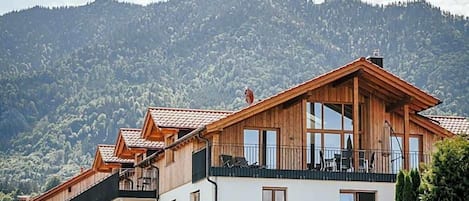 Um edifício de madeira com vários andares e varandas, com montanhas ao fundo.