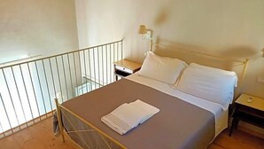 Een eenpersoonskamer met een metalen bedframe, een houten vloer, een nachtkastje en een lamp.