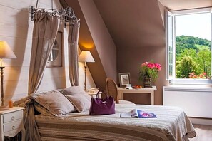 A bedroom with a bed, bedside lamps, a nightstand, a window with a view, and a chair. - Hostellerie Belle Rive (Gagnac-sur-Cere)