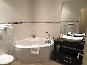 A modern bathroom with a corner bathtub, a white sink, and a black vanity. - Hostellerie Belle Rive (Gagnac-sur-Cere)