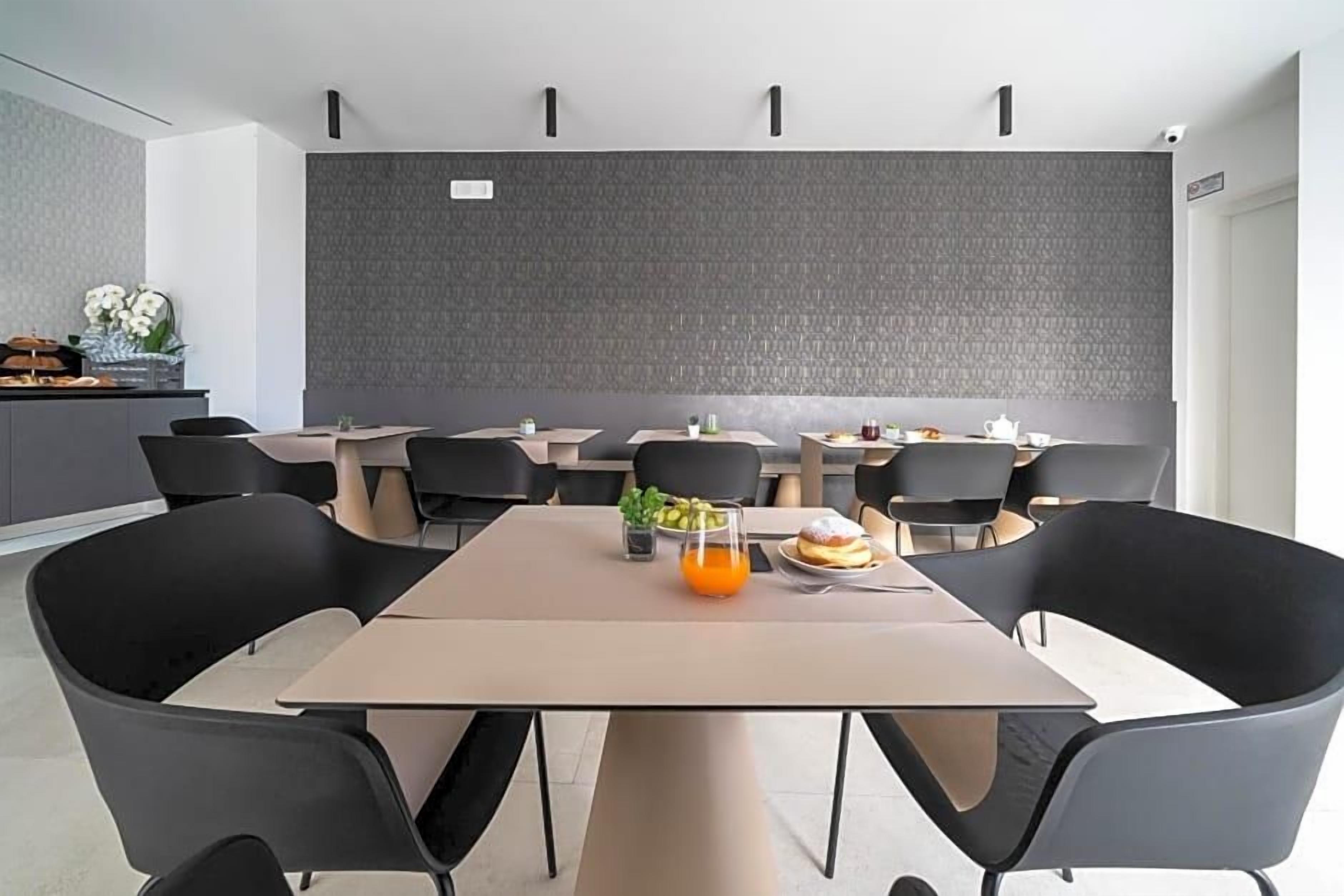 A modern dining area with multiple tables and chairs, a grey textured wall, and a small plant on one table.