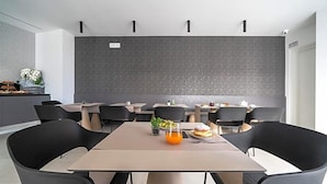A modern dining area with multiple tables and chairs, a grey textured wall, and a small plant on one table. - Comfort Zone (Codroipo)