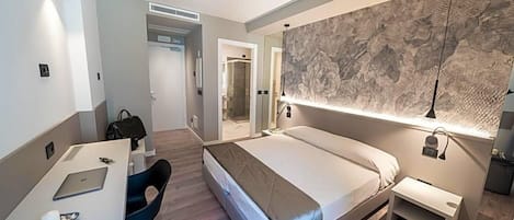 Una habitación de hotel moderna con una cama, un escritorio con una computadora portátil, una silla y un espejo grande.