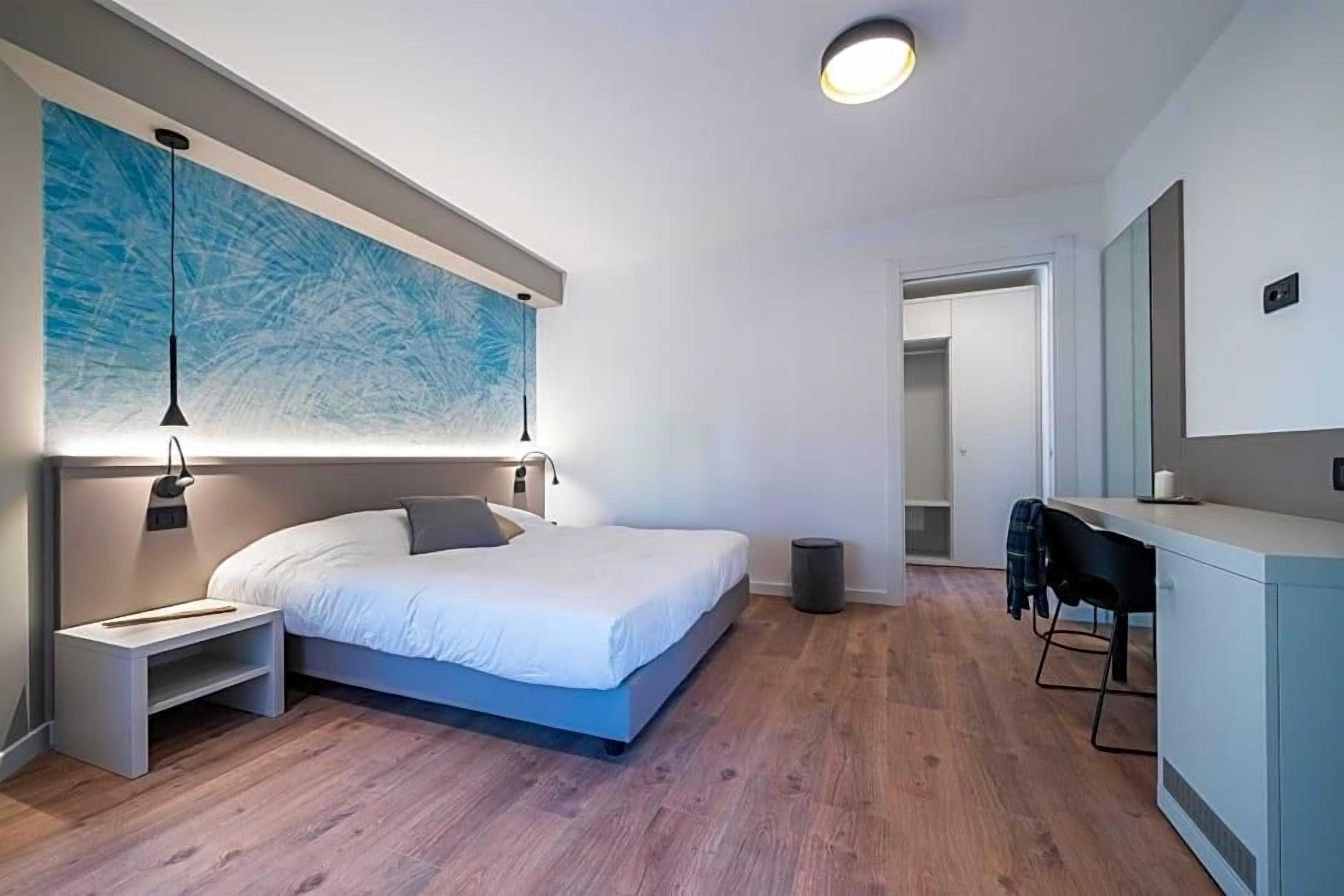A modern bedroom with a large bed, bedside tables, a desk, and a chair.