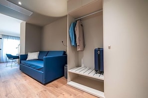 Ett modernt vardagsrum med en blå soffa, ett litet bord och en vit hylla med kläder och en resväska.
