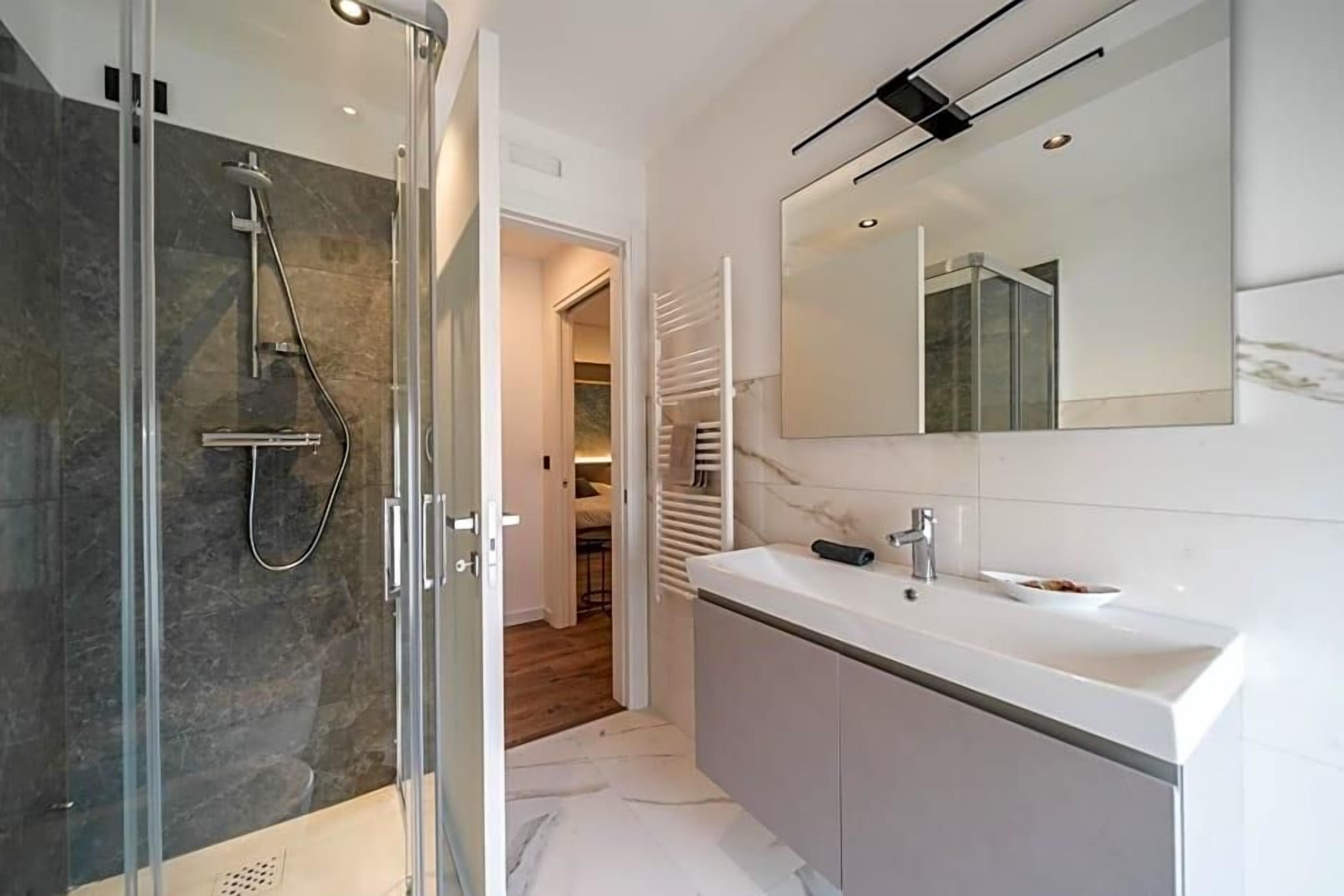 A modern bathroom with a glass-enclosed shower, a white vanity with a mirror, and a walk-in closet with a sliding door.
