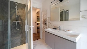 A modern bathroom with a glass-enclosed shower, a white vanity with a mirror, and a walk-in closet with a sliding door. - Comfort Zone (Codroipo)