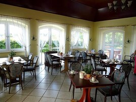 A dining area with multiple tables and chairs, large windows with curtains, and a tiled floor.