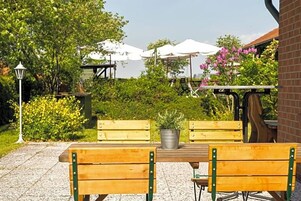 Un espace extérieur aménagé avec deux bancs en bois, un pot en métal contenant une plante et des parasols blancs.