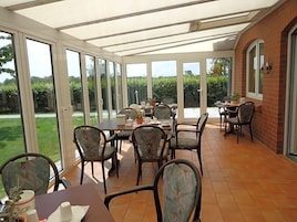 Un patio cubierto con mesa y sillas, ventanas amplias y una pared de ladrillo.