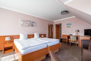 Una habitación de hotel con cama, mesita de noche, lámpara, escritorio, silla y televisor.