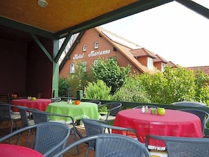 An outdoor patio area with tables and chairs, a brick building with 'Hotel Marianne' signage, and greenery in the background. - Hotel Marianne Und Restaurant Kiek In (Plau am See)