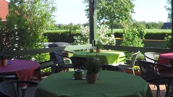 Un área de patio al aire libre con mesas redondas cubiertas con manteles verdes, rodeada de sillas.