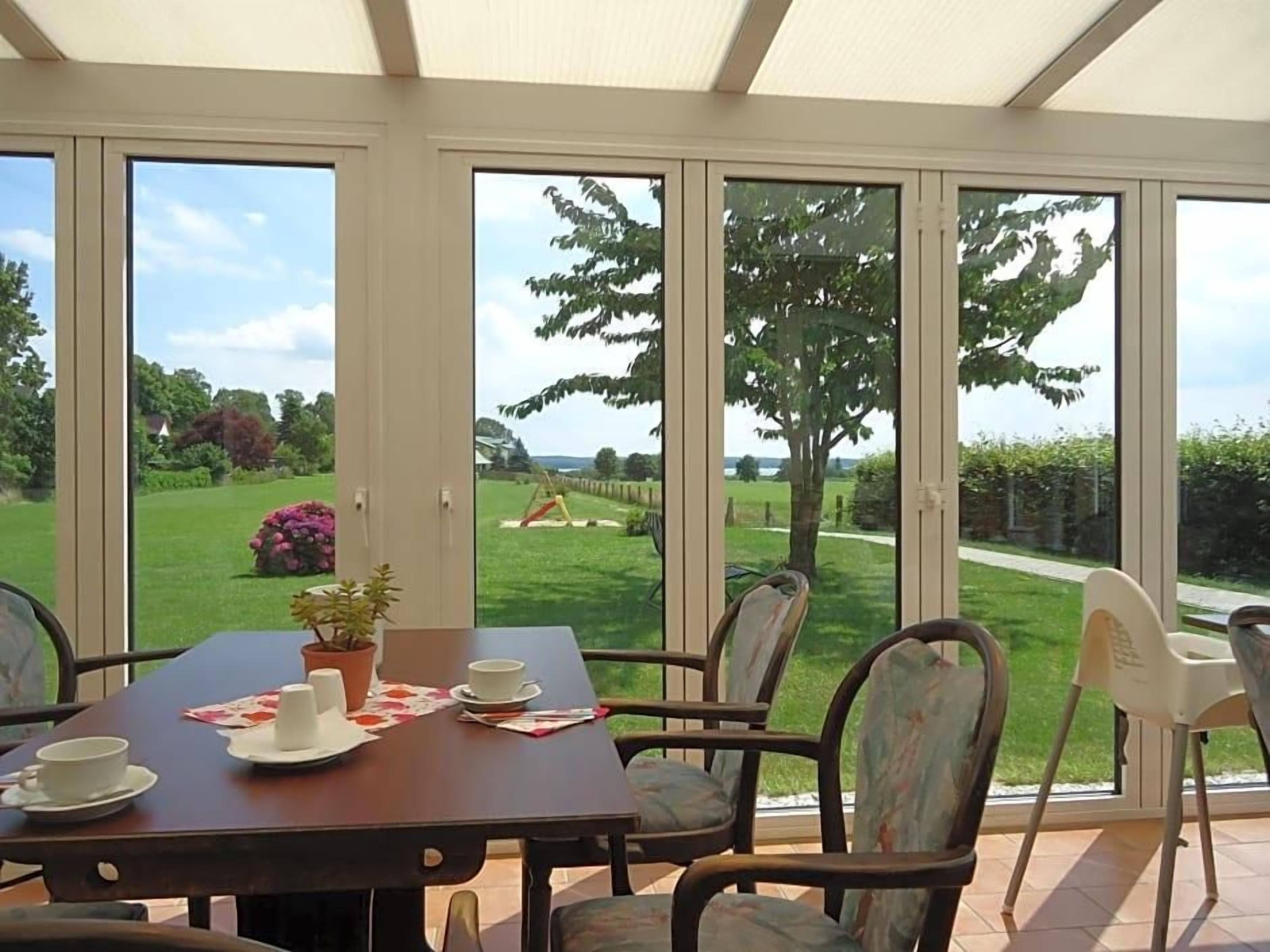 Ein Essbereich mit einem Tisch für zwei Personen, Stühlen und Blick auf einen Garten durch große Fenster.