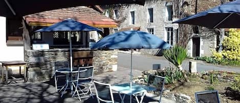 An outdoor seating area with tables and chairs under umbrellas, stone walls, and a building in the background.