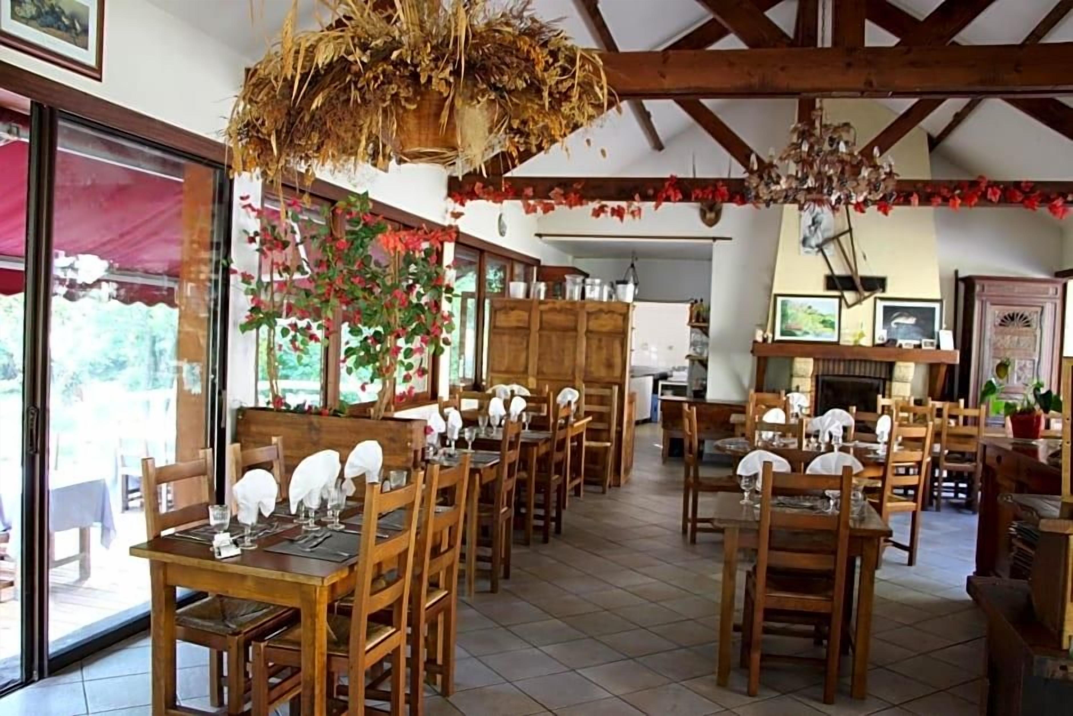 Un comedor con mesas y sillas de madera, una araña y vistas amplias a través de grandes ventanas.