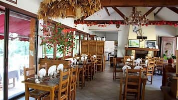 Un comedor con mesas y sillas de madera, una araña y vistas amplias a través de grandes ventanas.
