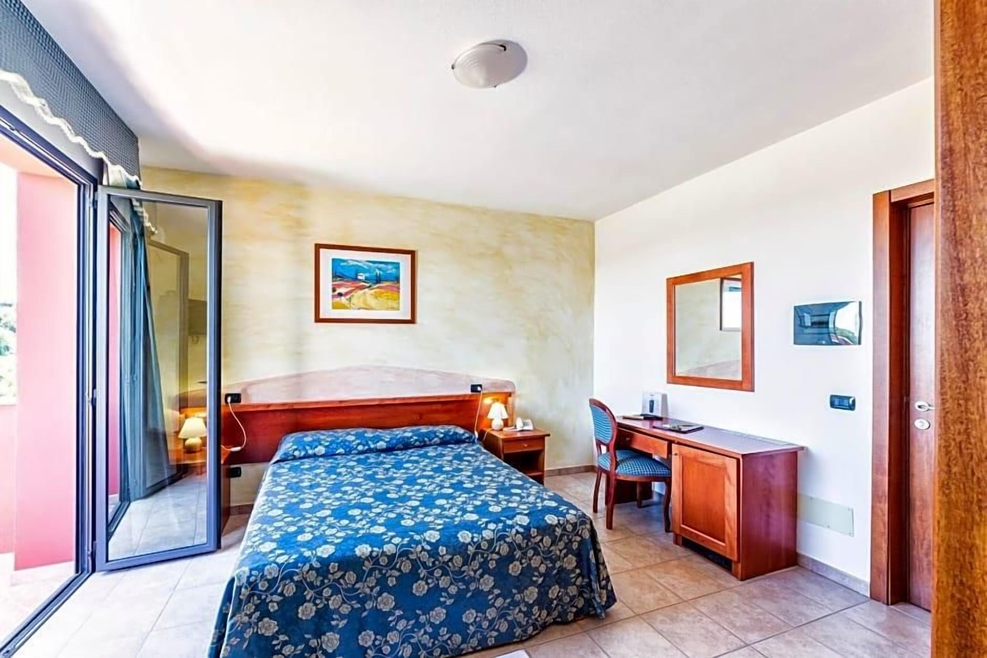 Un dormitorio con cama, escritorio, silla, ventana y puerta.