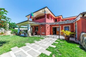 Um edifício vermelho com varanda coberta e caminho de pedra até a entrada.