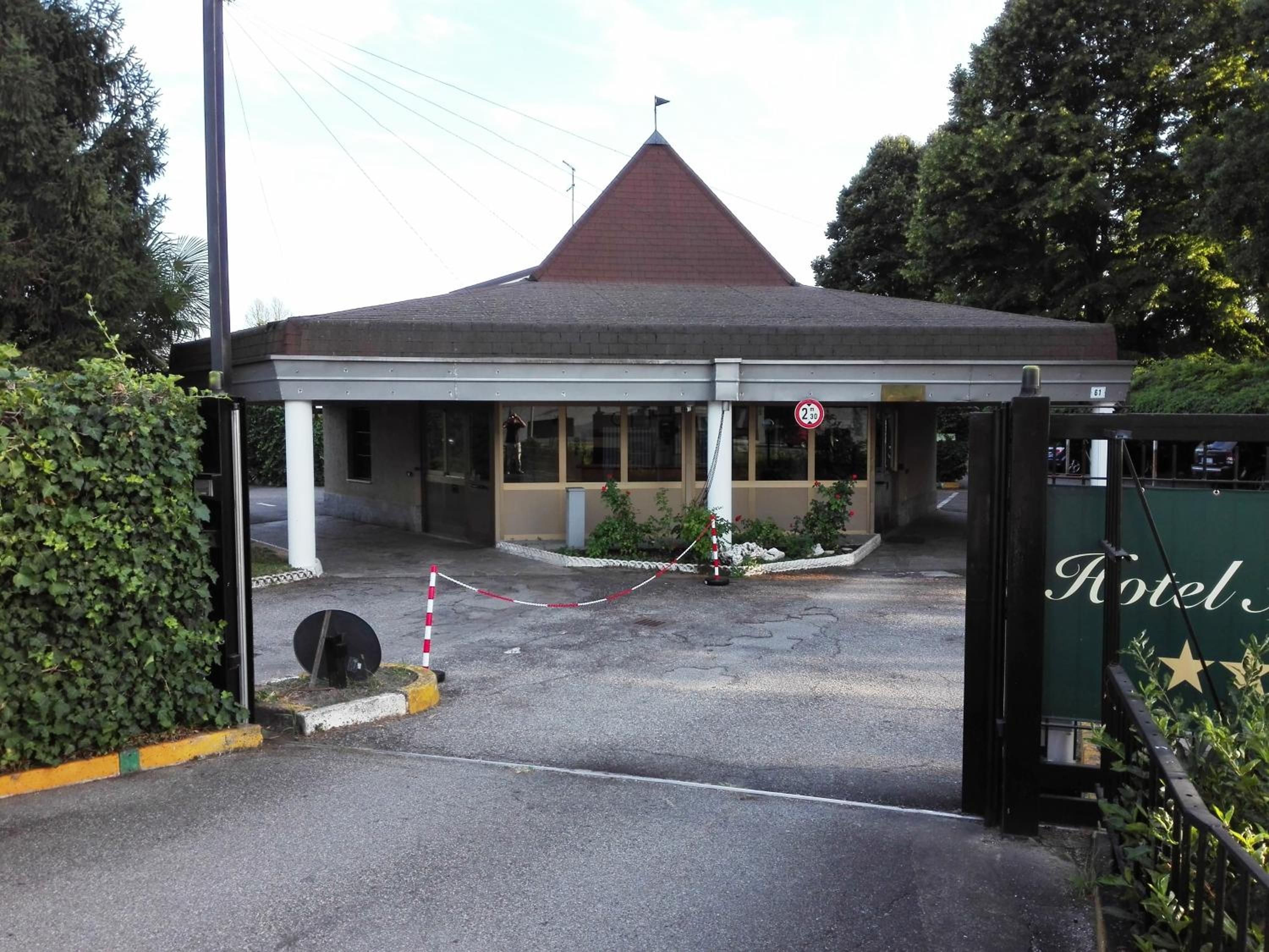 Entrada de un hotel con un camino de acceso empedrado, una zona de espera techada y un cartel que indica una distancia de 2.3 kilómetros.