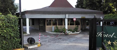 Entrada de un hotel con un camino de acceso empedrado, una zona de espera techada y un cartel que indica una distancia de 2.3 kilómetros.
