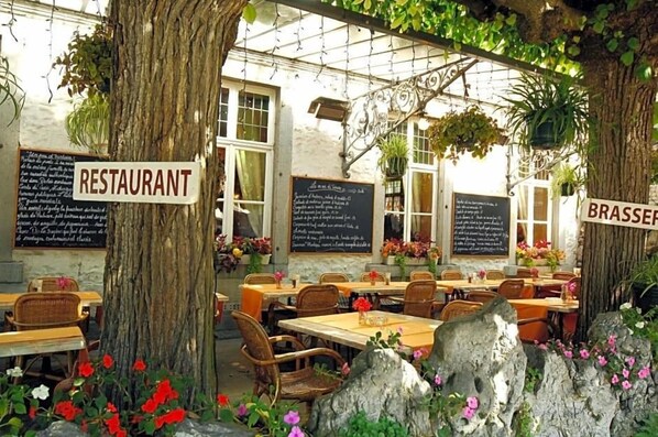 An outdoor restaurant with tables and chairs, surrounded by trees and flowers.